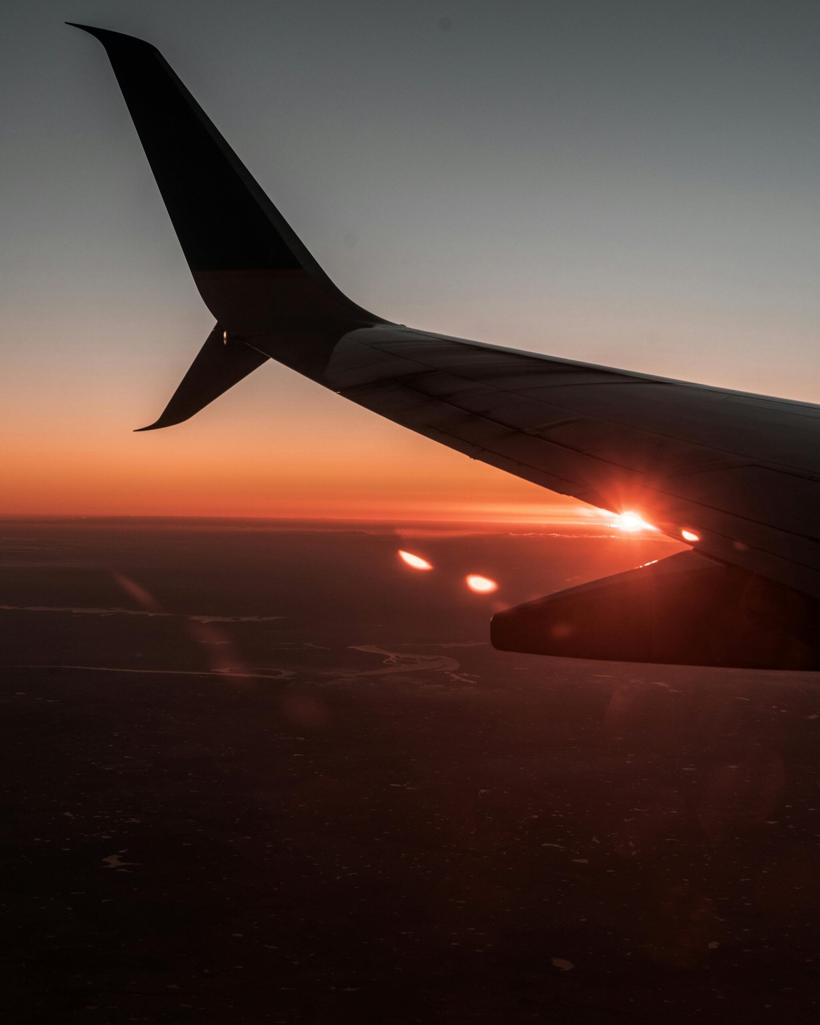 A dramatic view of an airplane wing silhouetted against a vibrant sunset sky, capturing the essence of travel.