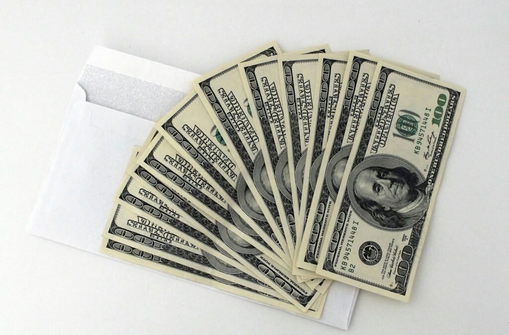 Fan of US $100 bills partially out of a white envelope on a white background.